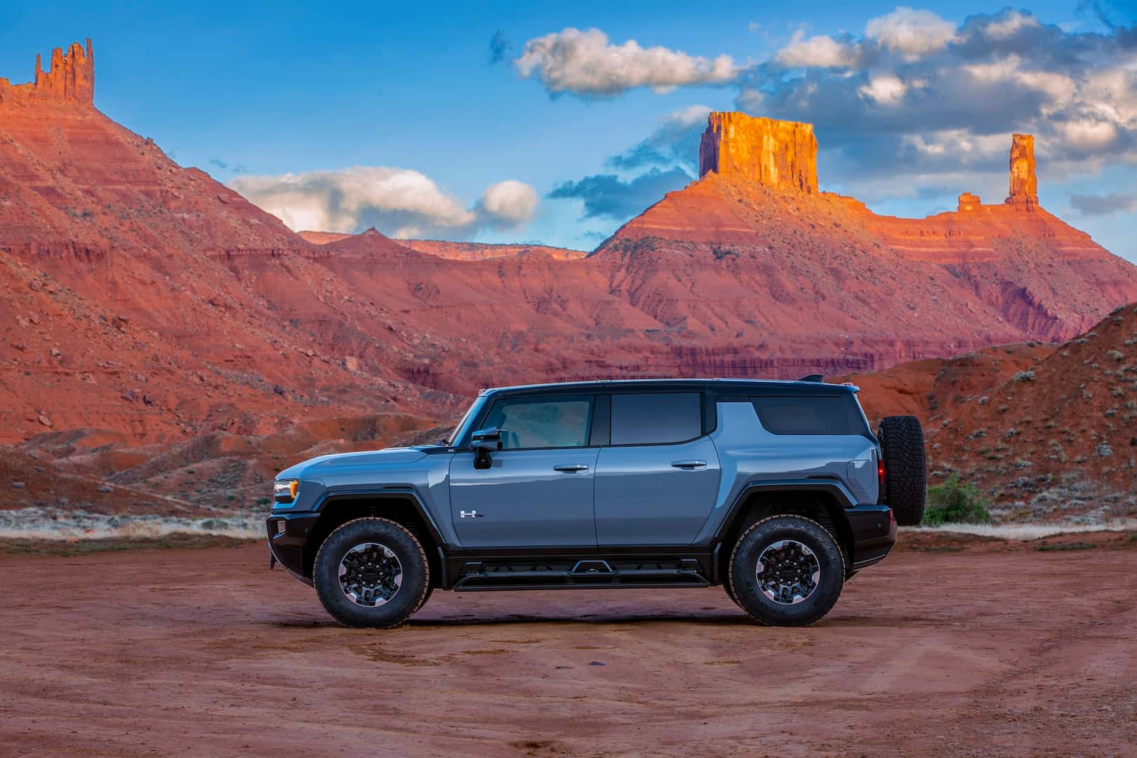 Side view of 2024 GMC HUMMER EV SUV 3X in Meteorite Metallic with desert mountain backdrop.