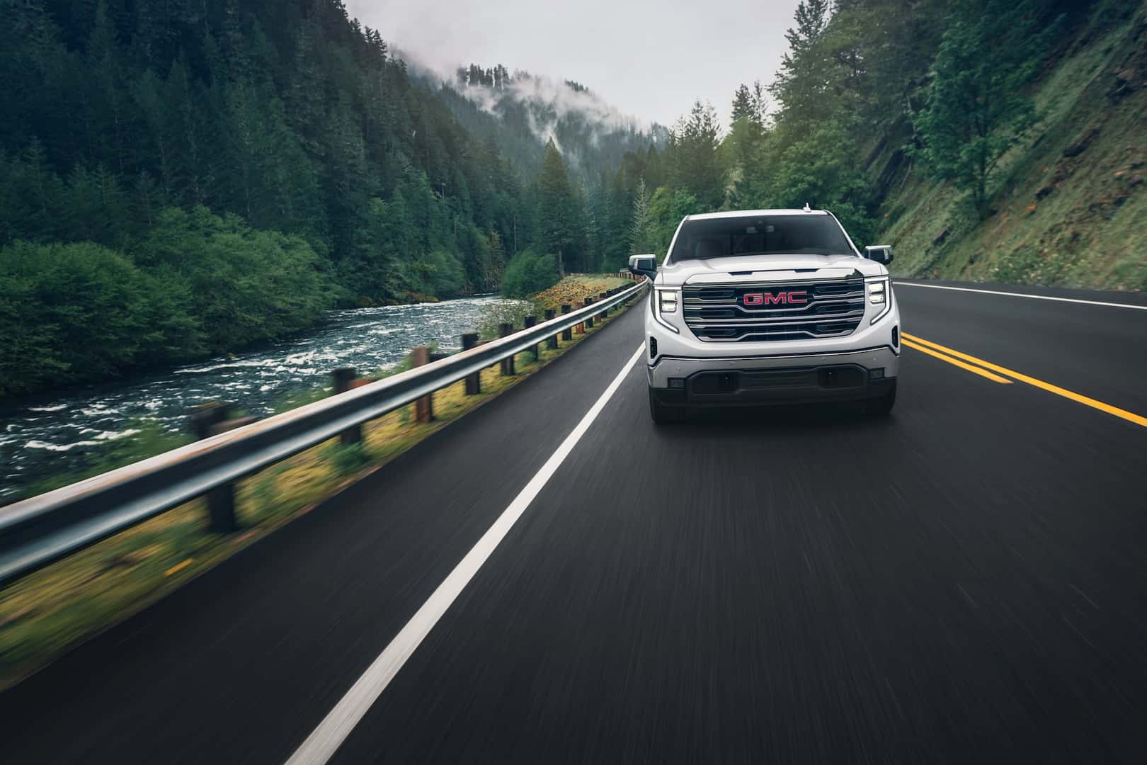 2024 GMC Sierra 1500 SLT Crew Cab Short Box 4WD in White Frost Tricoat. Direct front image in motion, driving on bridge next to river.