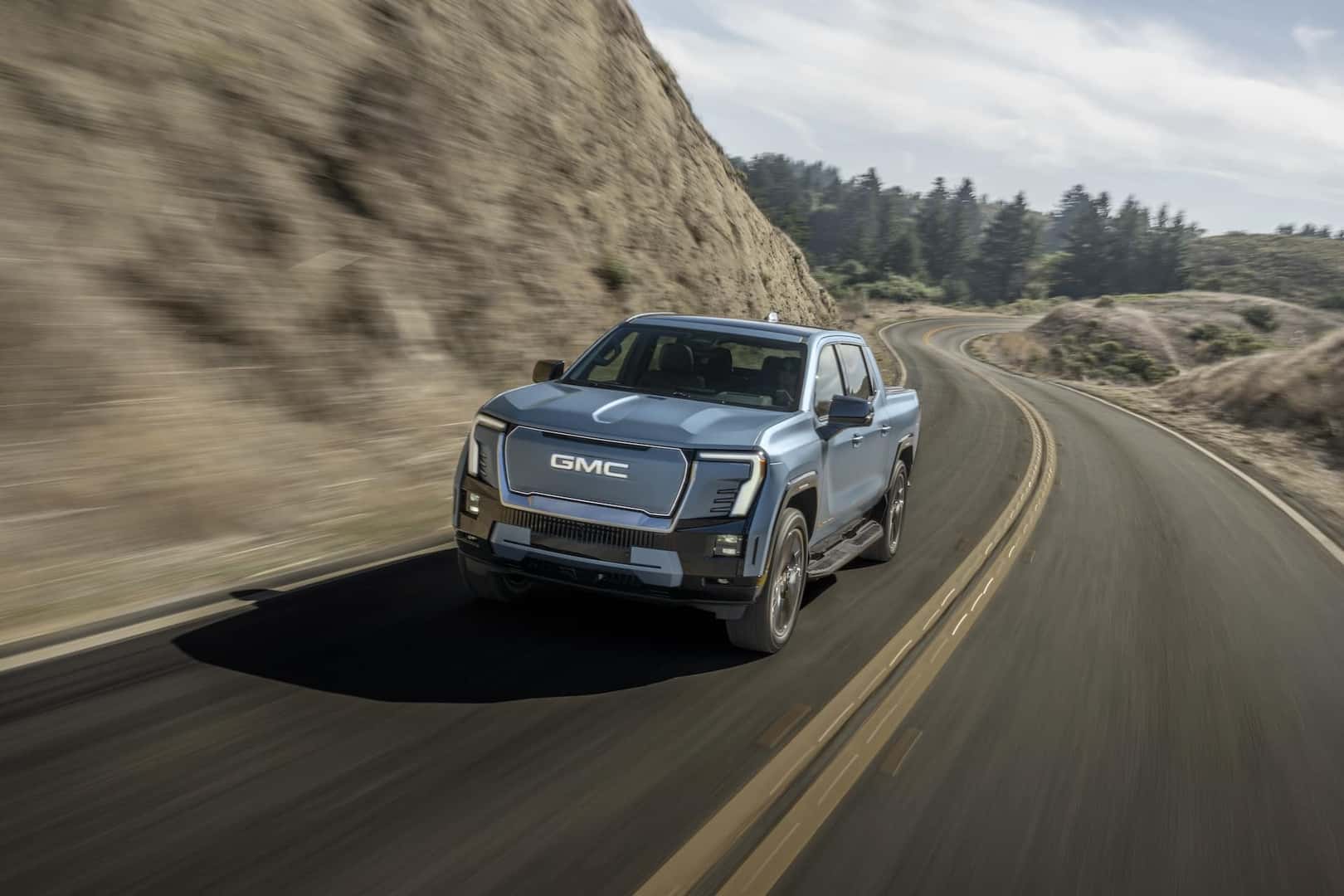 Front shot of the 2025 GMC Sierra EV Denali in Moonlight Matte driving on mountain road.