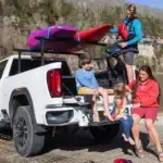 2026 GMC Life Adventure Truck Bed with accessories, kayaks and a family by a lake