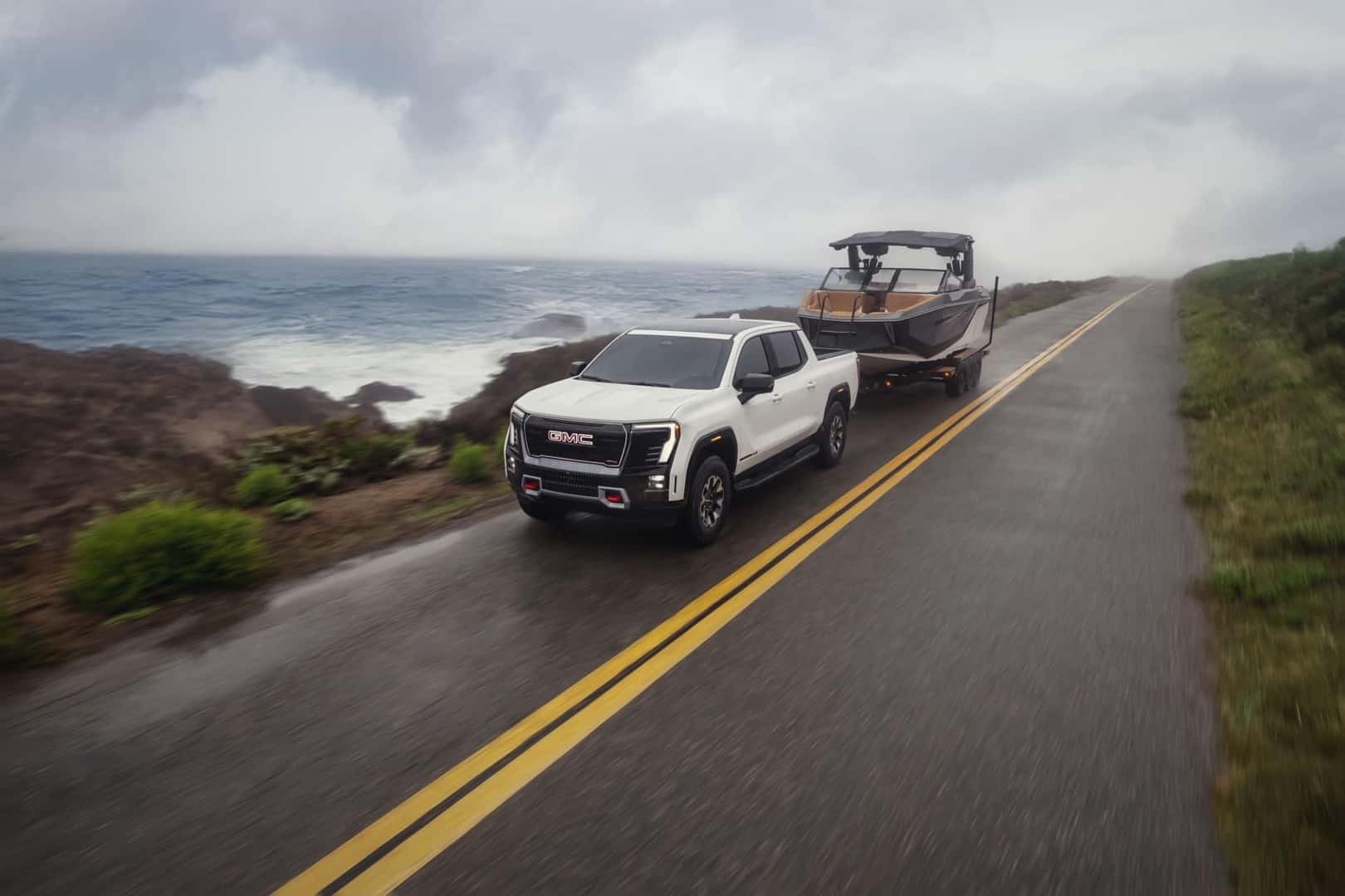 The 2026 GMC Sierra EV AT4 Towing A Boat On A Wet Road Under A Cloudy Sky